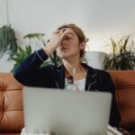 Zmęczona kobieta z drinkiem przy laptopie, zestresowana planowaniem ślubu
